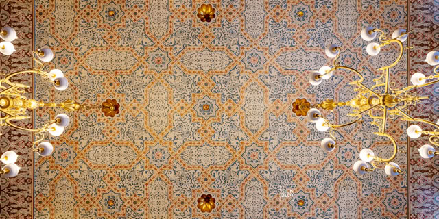 Dekorative Decke mit symmetrischem Muster und zwei großen, verzierten Kronleuchtern.