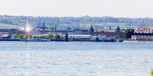 Blick auf Konstanz Stadt am Wasser mit historischen Gebäuden und grüner Landschaft im Hintergrund.