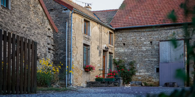 Steinhaus mit roten Ziegeldächern, Blumen vor den Fenstern und einem Kiesweg im Vordergrund.